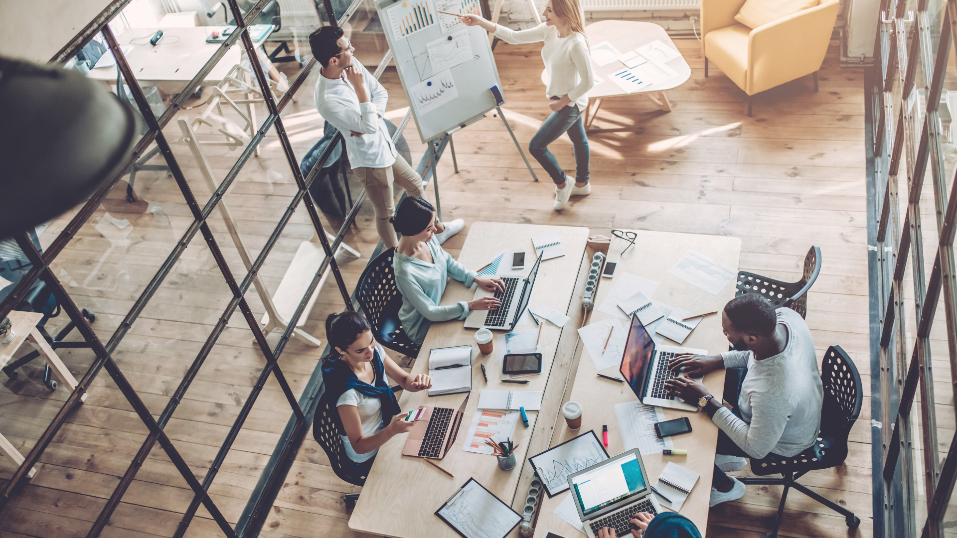 An overhead view of a bustling, modern open-plan office with employees working on laptops